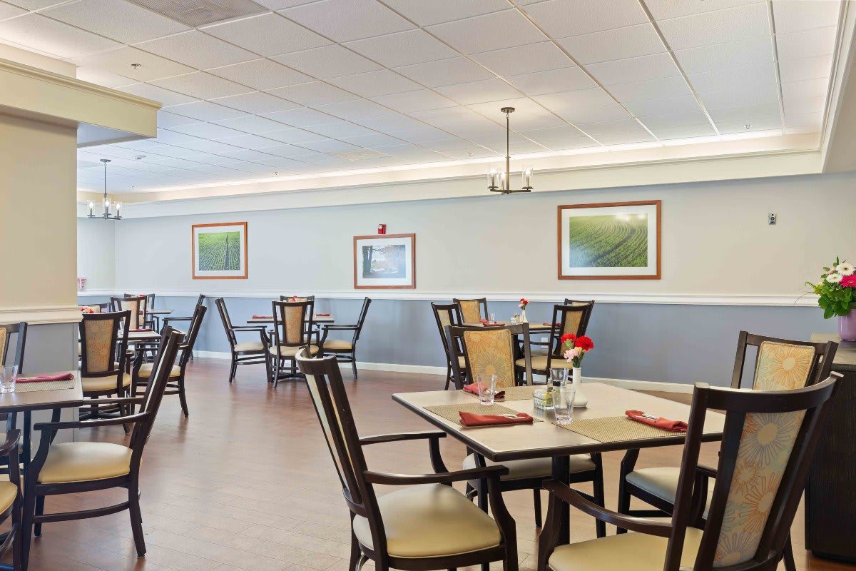 A spacious and well-decorated dining room with neatly arranged tables and chairs, adorned with flowers and framed pictures on the walls.