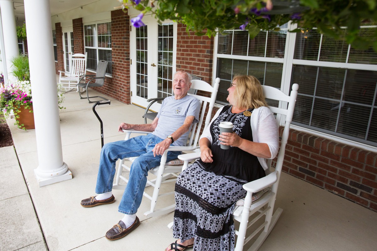 An elderly couple enjoying a conversation on a porch while sitting in rocking chairs.