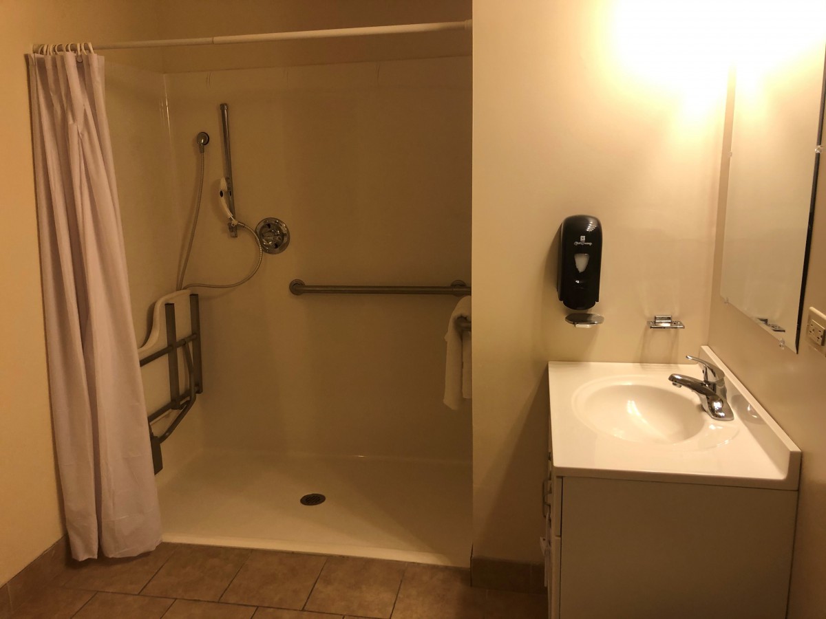 An accessible bathroom featuring a walk-in shower with grab bars and a single sink.