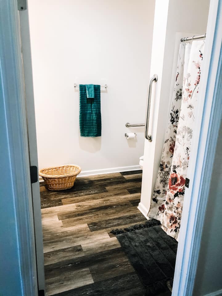 A minimalist bathroom with a floral shower curtain and wooden flooring.