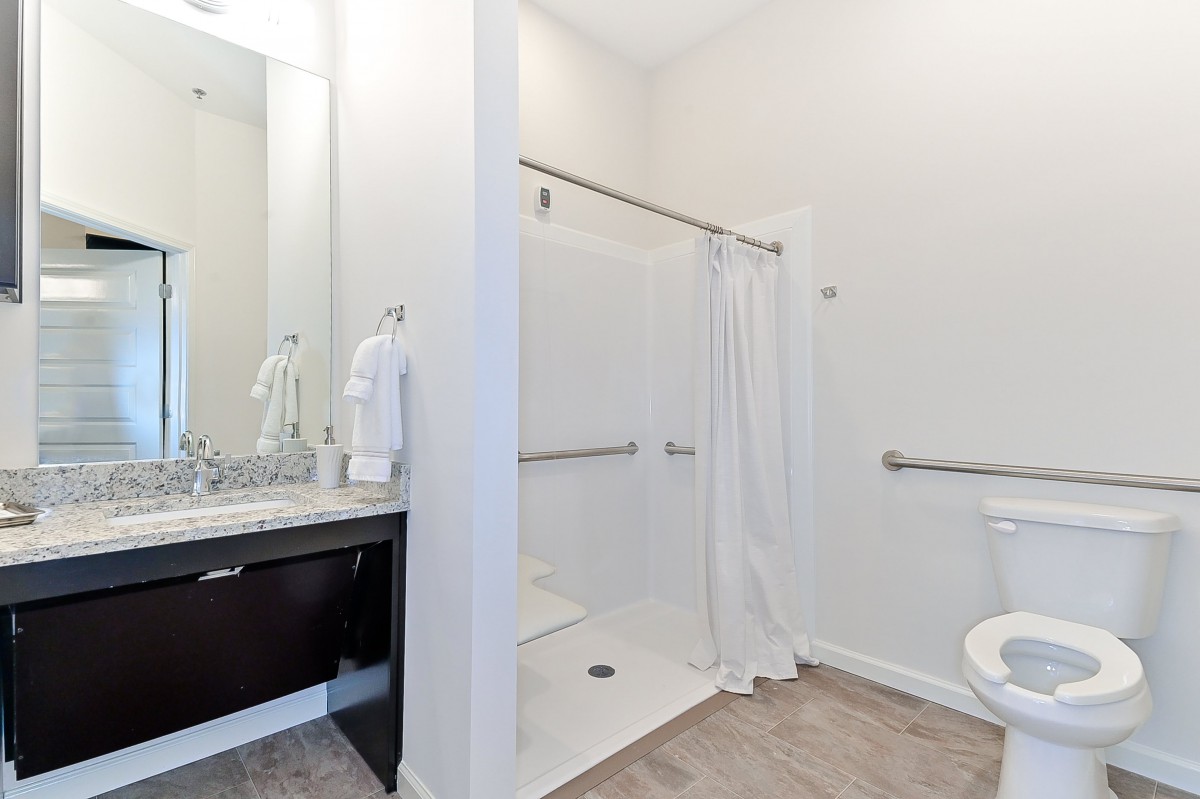 A modern bathroom featuring a walk-in shower with white tiles and a curtain, complemented by a sleek sink and mirror setup.