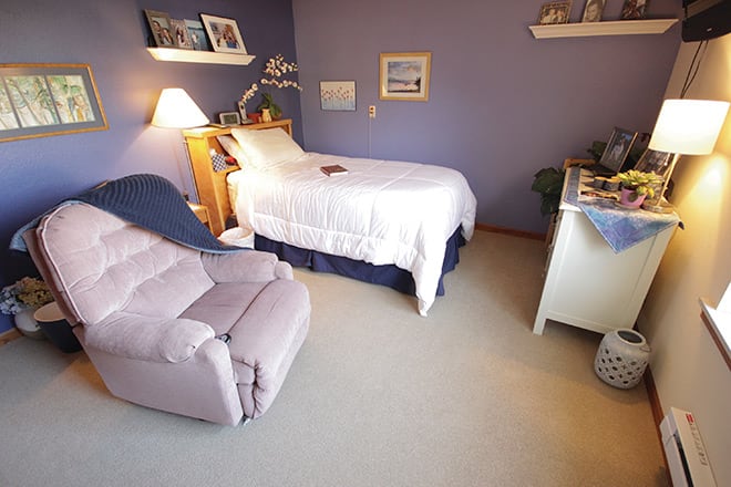 A cozy bedroom with a bed, recliner, and soft lighting.