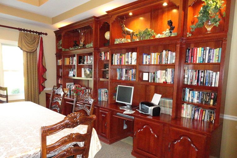A home library and office space featuring elegant wooden bookshelves filled with books, a desk with a computer, and comfortable chairs.
