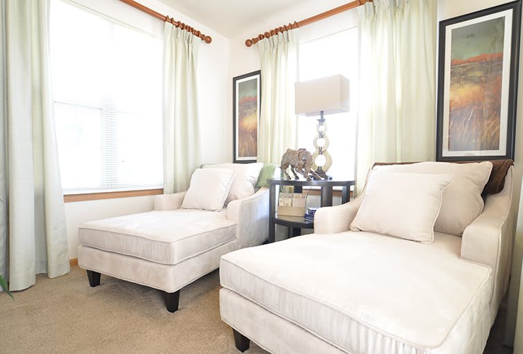 A cozy living room corner with two white armchairs, a side table with a lamp, and light green curtains.
