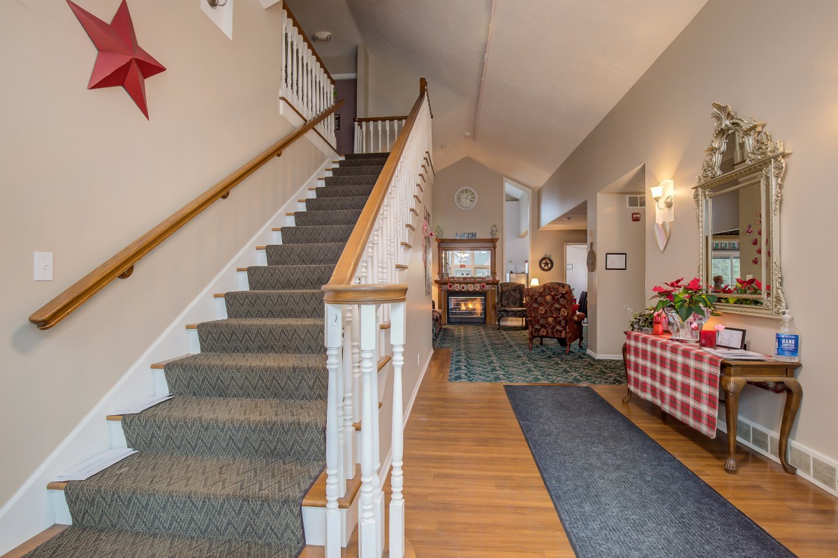 A cozy home interior with a staircase leading upwards, featuring a carpeted floor, wooden accents, and a warm fireplace in the background.