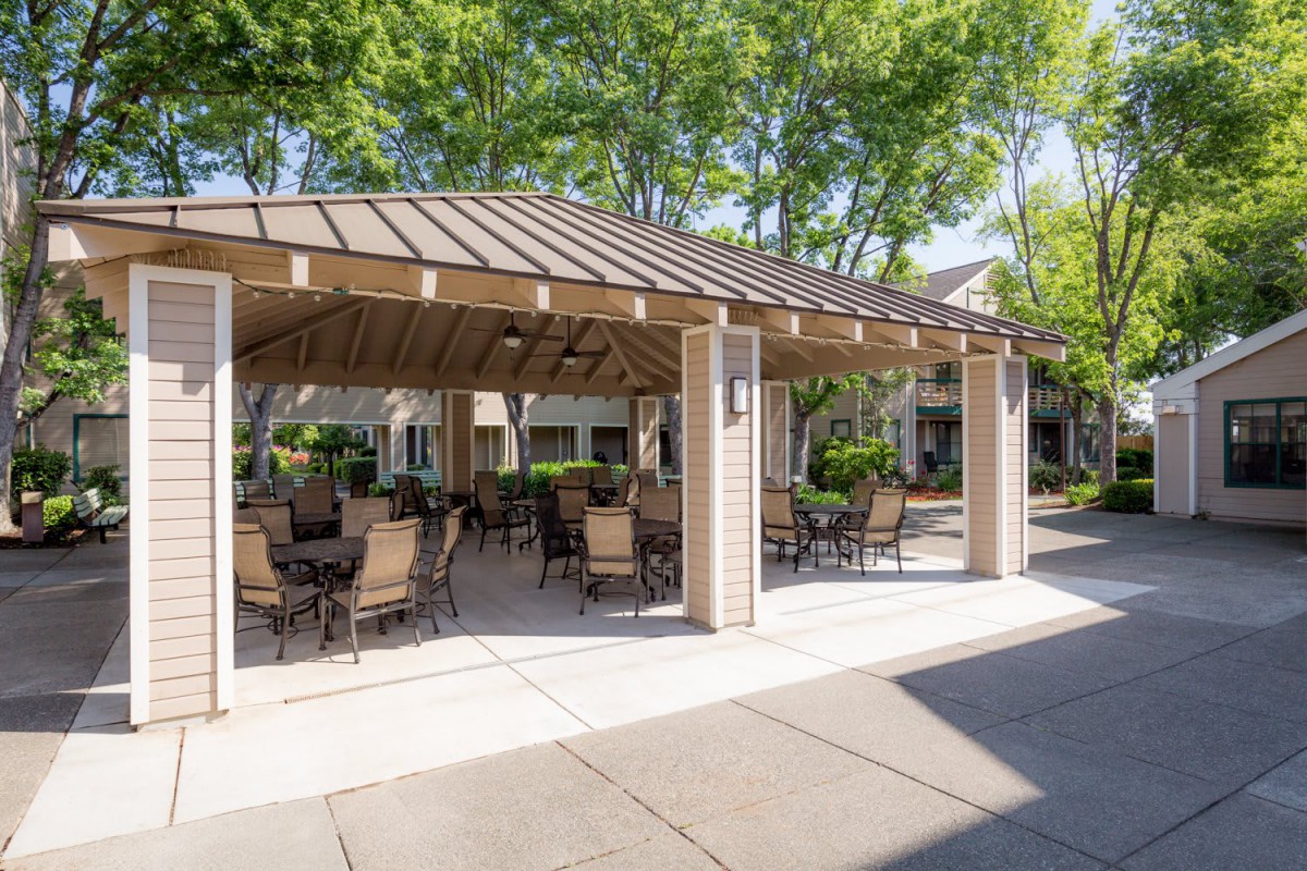 A spacious outdoor seating area under a wooden gazebo in a lush garden setting.