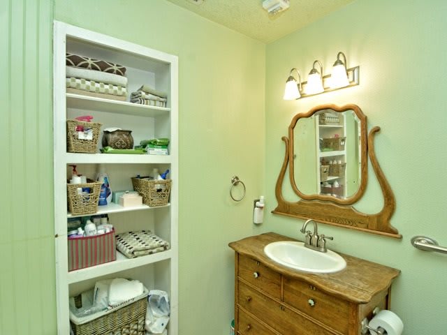 A well-organized bathroom with a wooden vanity, large mirror, and neatly arranged shelving.