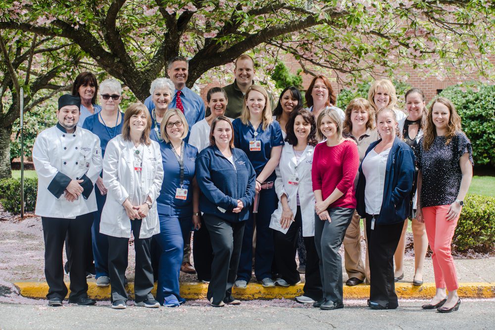 A group of people smiling together outdoors under a tree.