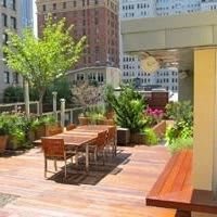 A cozy urban rooftop terrace with outdoor seating, surrounded by lush plants and city buildings.