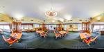 A spacious banquet hall with elegant chandeliers, neatly arranged tables and chairs, and a decorative carpet.