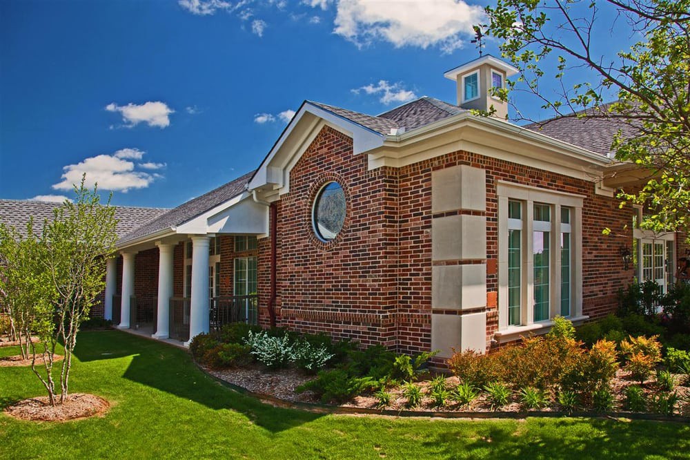 A beautifully designed brick house with well-maintained landscaping under a clear blue sky.