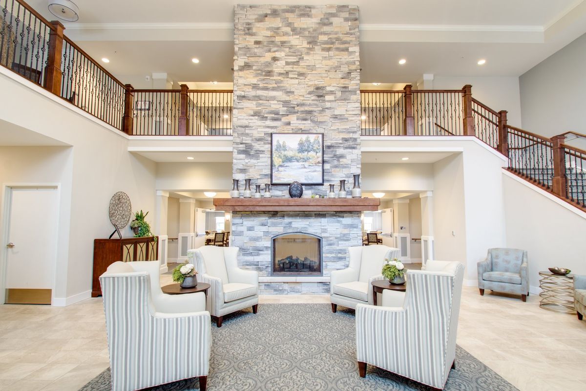 A spacious modern living room featuring a central fireplace with striped armchairs and elegant decor.