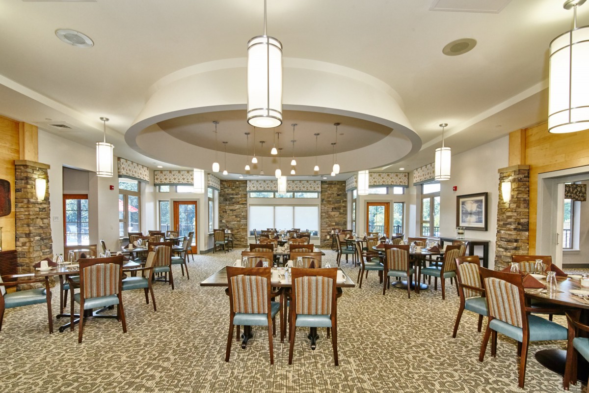 A spacious dining area with neatly arranged tables and chairs, featuring elegant lighting fixtures and large windows.