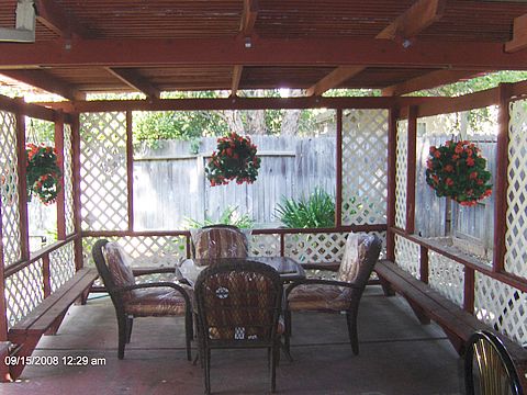 A cozy outdoor patio area with lattice walls, featuring a table and chairs under a pergola.