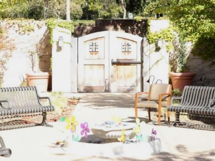 A sunny outdoor seating area with chairs near a decorative gate surrounded by plants.
