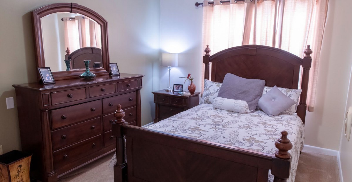 A cozy bedroom with a wooden bed and dresser, softly lit by a bedside lamp.