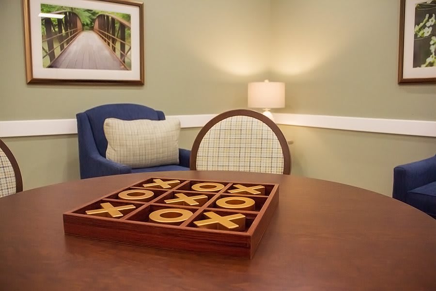 A cozy room with a tic-tac-toe board game on the table, surrounded by chairs and warm lighting.