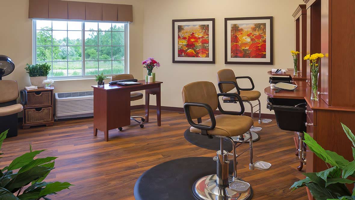 A cozy salon interior featuring styling chairs, a desk with flowers, and decorative paintings on the wall.