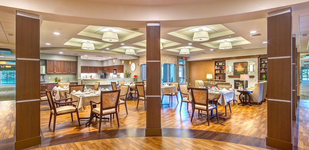 A modern restaurant interior with neatly arranged tables and chairs, elegant lighting, and a warm wooden floor.