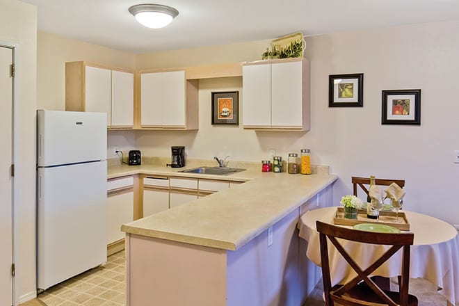 A modern kitchen and dining area with light-colored cabinets, a refrigerator, and a small dining table.