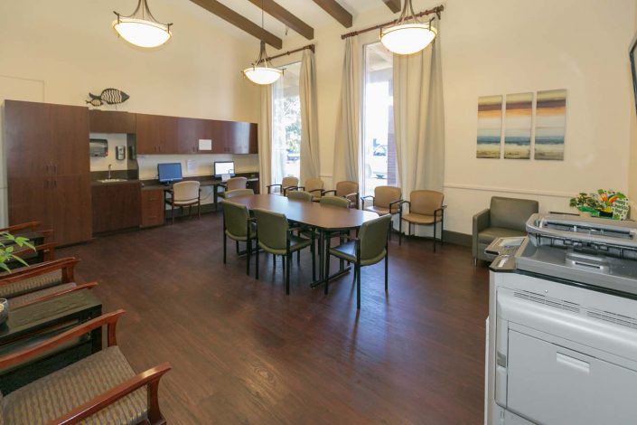 A spacious meeting room with a large table, chairs, and computer stations, featuring high ceilings and wooden flooring.