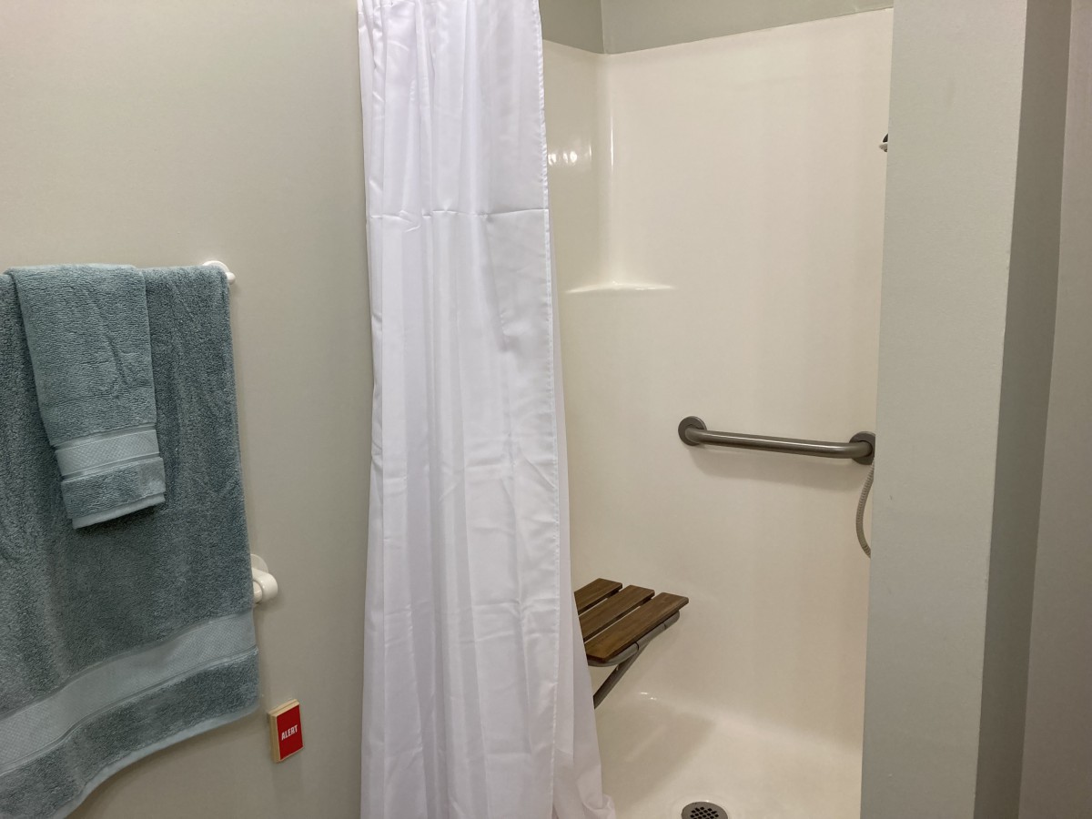 An accessible bathroom shower with a white curtain, grab bar, and bench.