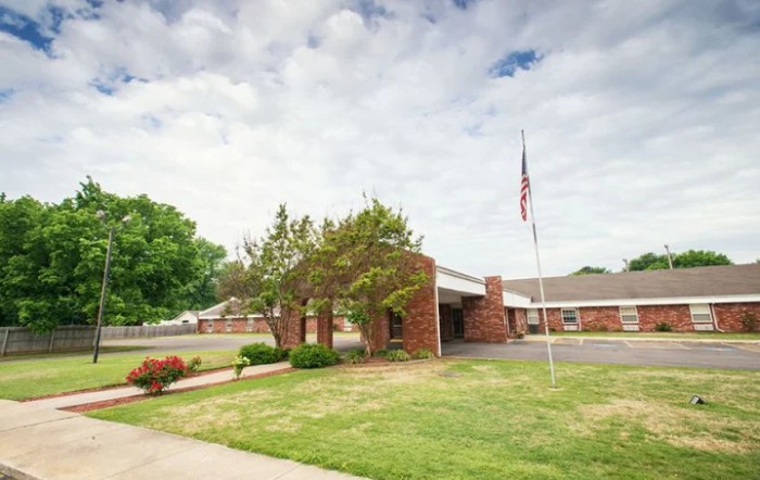 A brick building with an entrance, surrounded by greenery and a flagpole, under a cloudy sky.