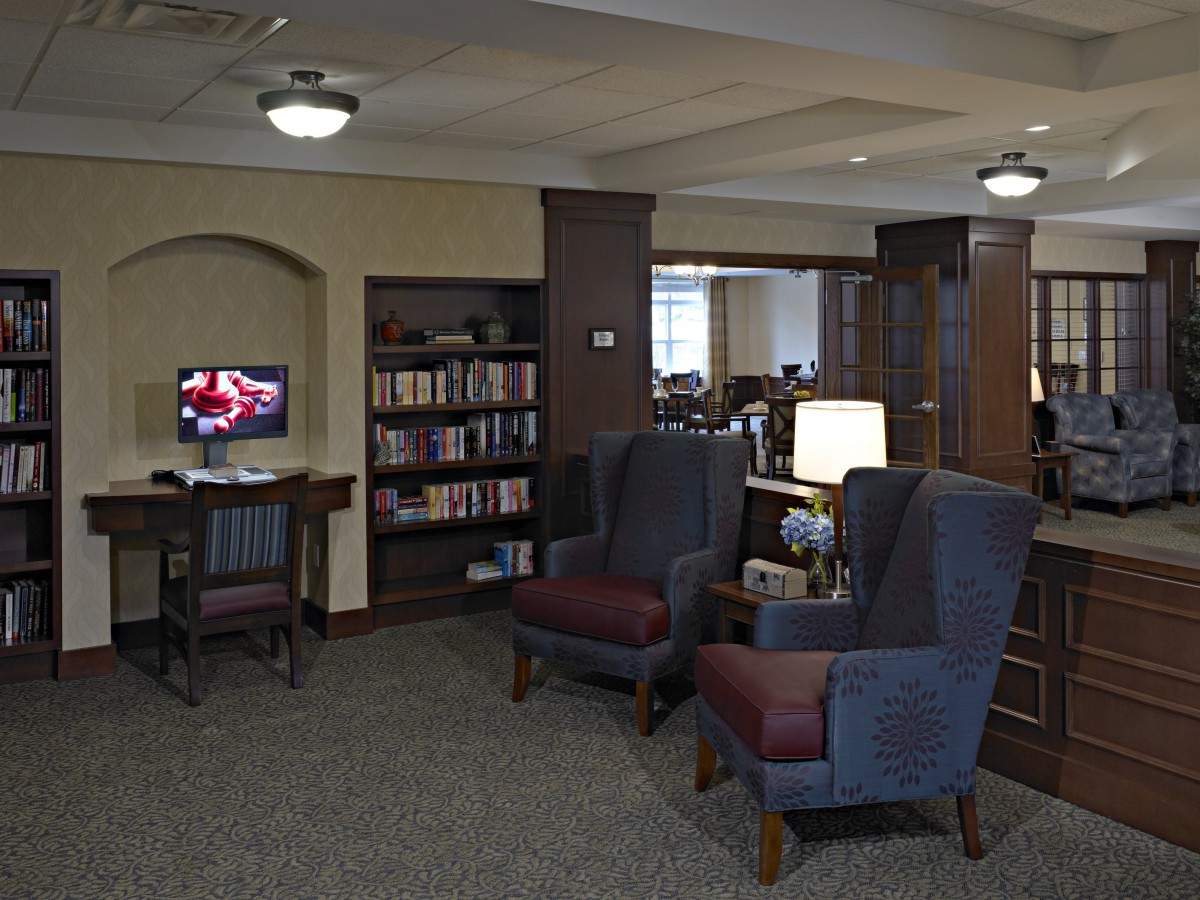 A cozy library nook featuring bookshelves, armchairs, and a computer station.