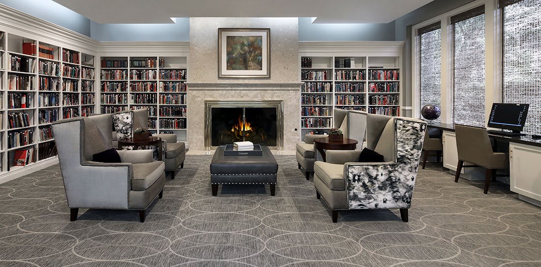A cozy library setting with a fireplace, surrounded by bookshelves and comfortable armchairs.