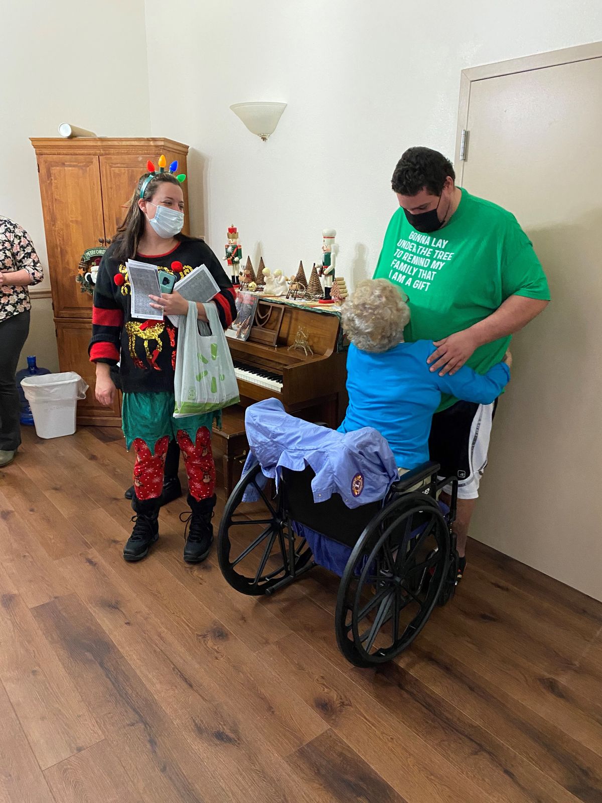 A heartwarming moment as a person in a wheelchair hugs another, while someone in a colorful costume looks on.