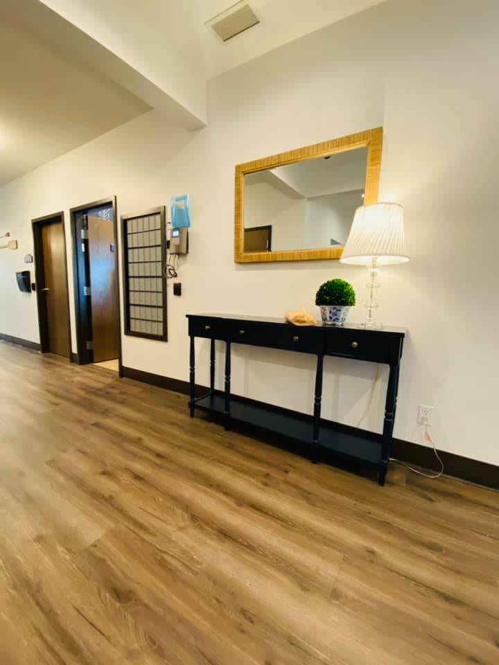 A modern hallway with a wooden floor, featuring a sleek black console table adorned with decorative items, a lamp, and an elegant mirror on the wall.