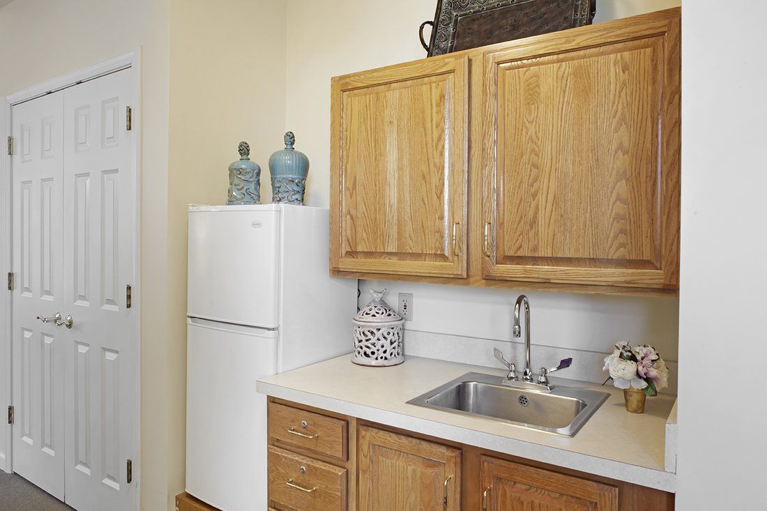 A small kitchen area featuring wooden cabinets, a white refrigerator, and a sink on the countertop with decorative items.