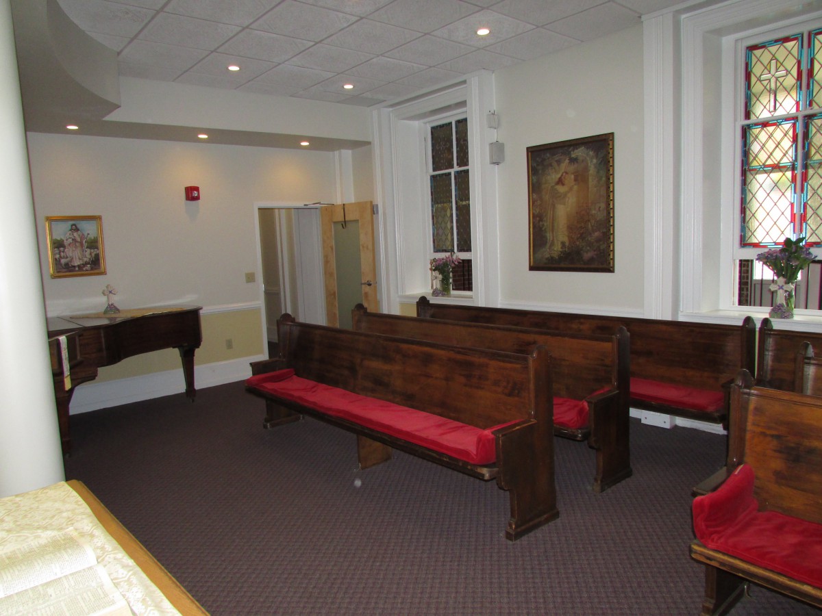 A small church interior with wooden pews, a piano, and a painting on the wall.