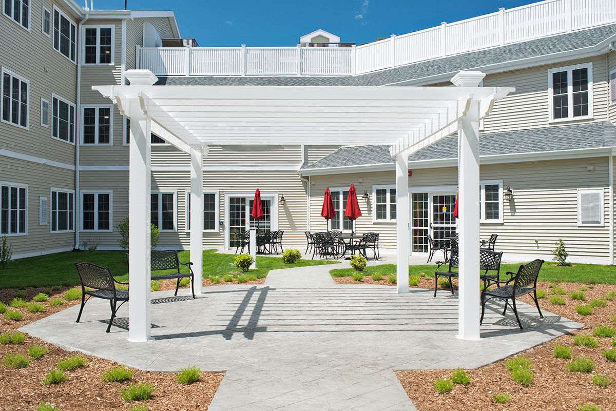A scenic outdoor patio area with a pergola, surrounded by tables and chairs in front of a building.