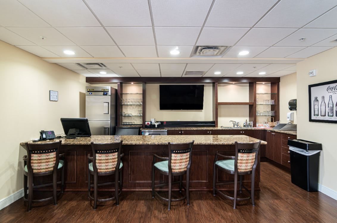 An empty bar with a granite countertop and chairs, featuring a television on the wall.
