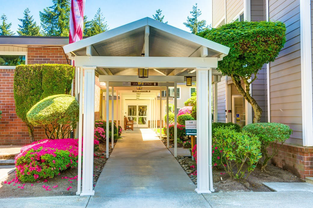 A covered walkway leading to a building entrance, surrounded by well-maintained gardens.