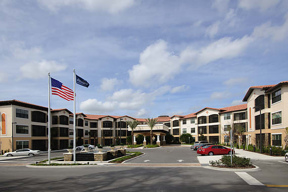 A hotel building with flags and a parking lot under a cloudy sky.