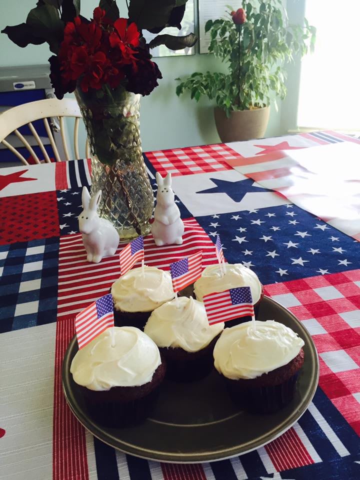Patriotic cupcakes adorned with American flags on a red, white, and blue table setting.