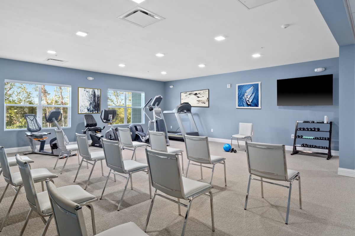 A multi-purpose room with exercise equipment and arranged chairs for a meeting or class.