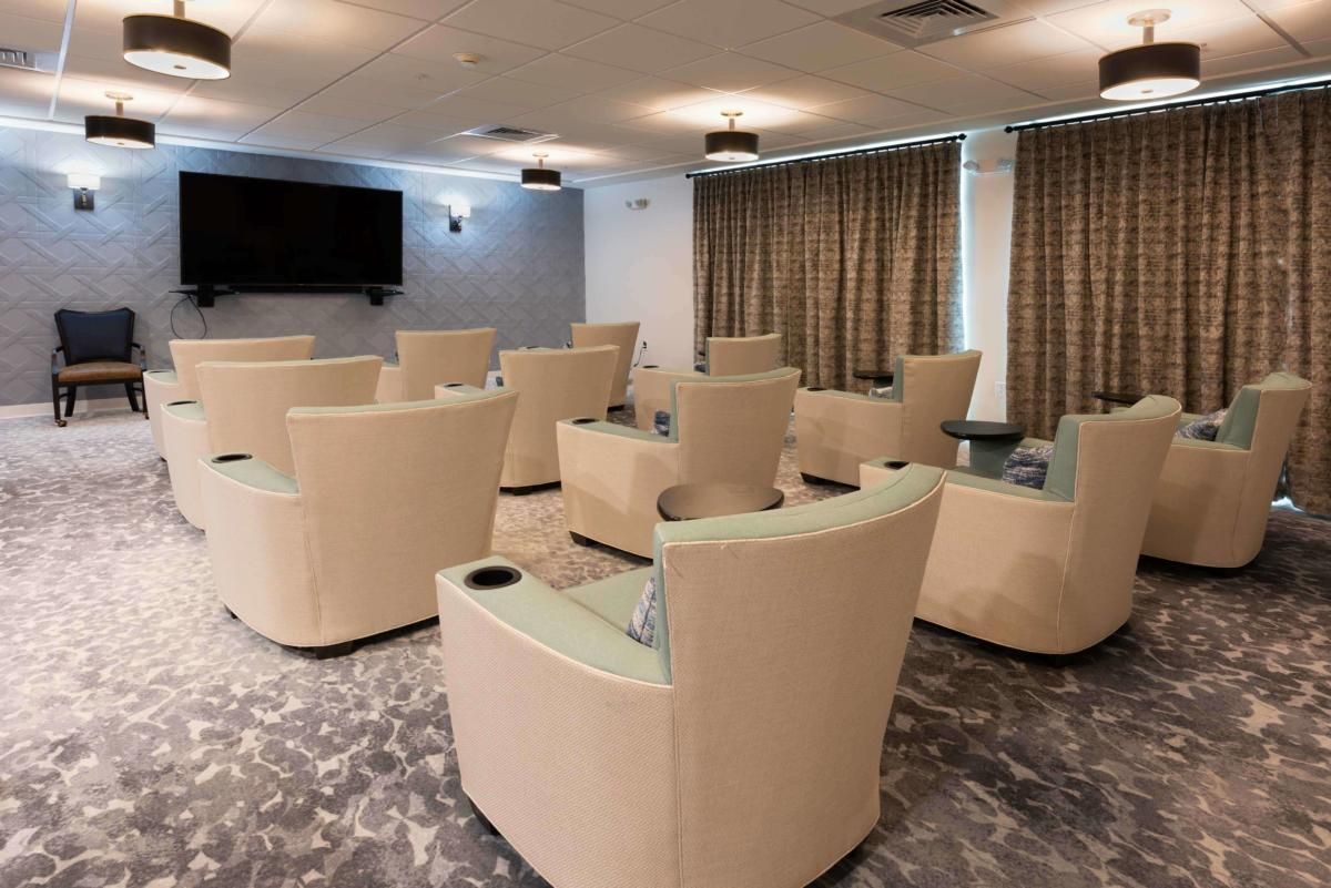 A cozy theater room with rows of comfortable beige chairs facing a large screen.
