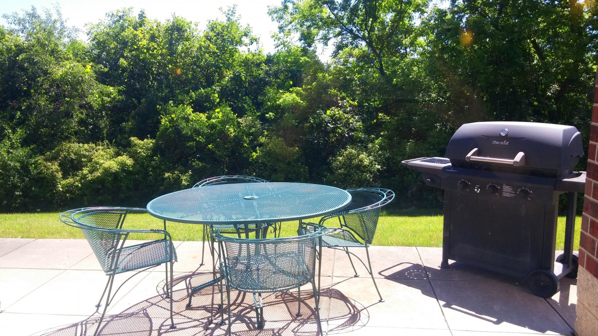 A sunny backyard patio with a table, chairs, and a grill.