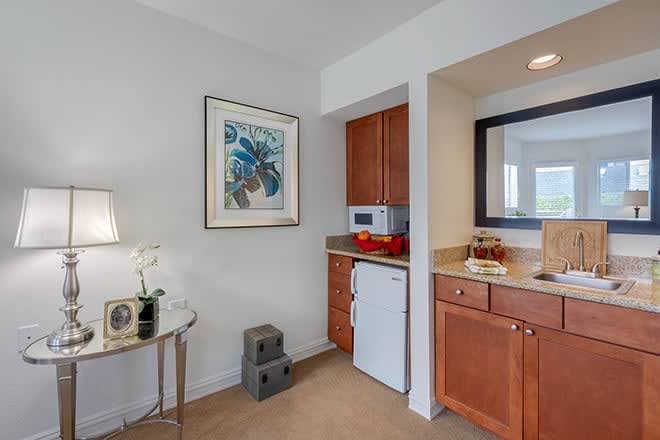 A compact kitchenette with wooden cabinetry, featuring a microwave, refrigerator, and decorative elements.