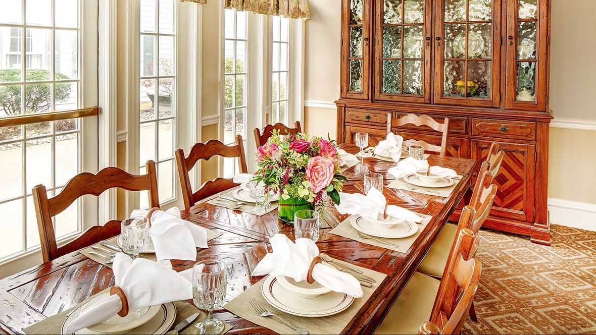 A beautifully set dining table in a bright, elegant room with wooden furniture and floral centerpiece.