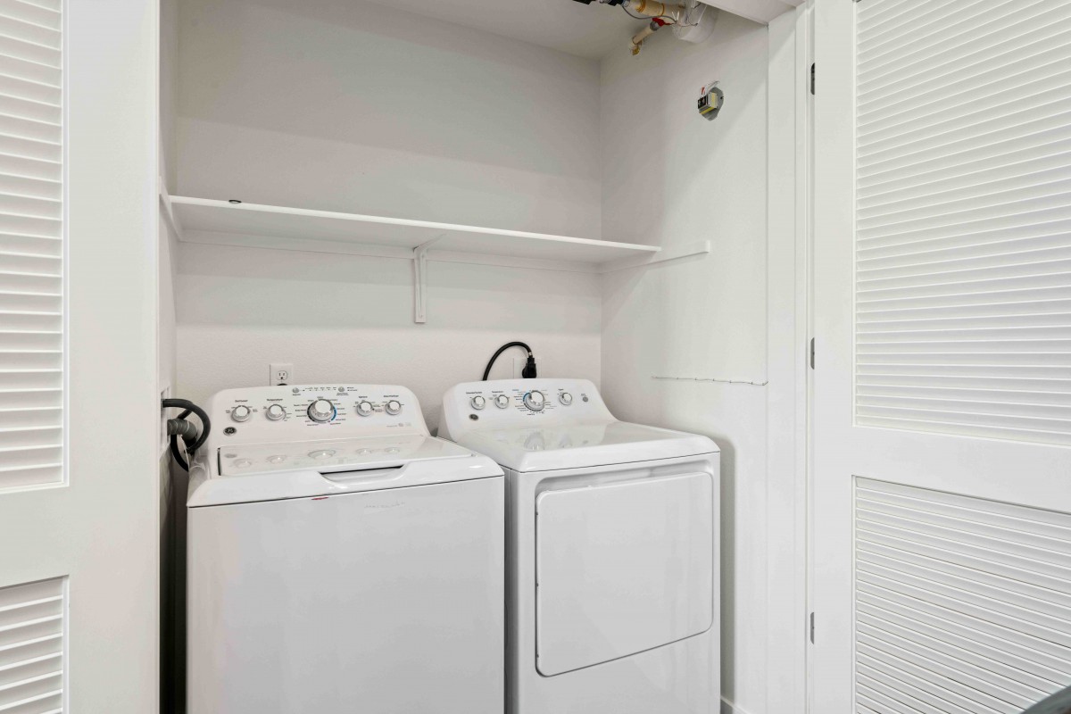 A compact laundry room with a washing machine and dryer side by side, beneath a shelf.