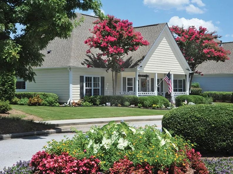 A charming suburban house surrounded by a well-maintained garden with colorful flowers and trees.