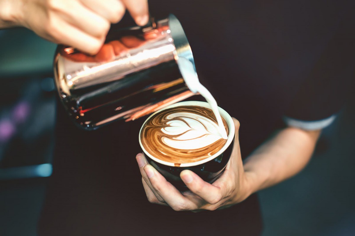 A barista skillfully creates latte art by pouring milk into a cup of coffee.
