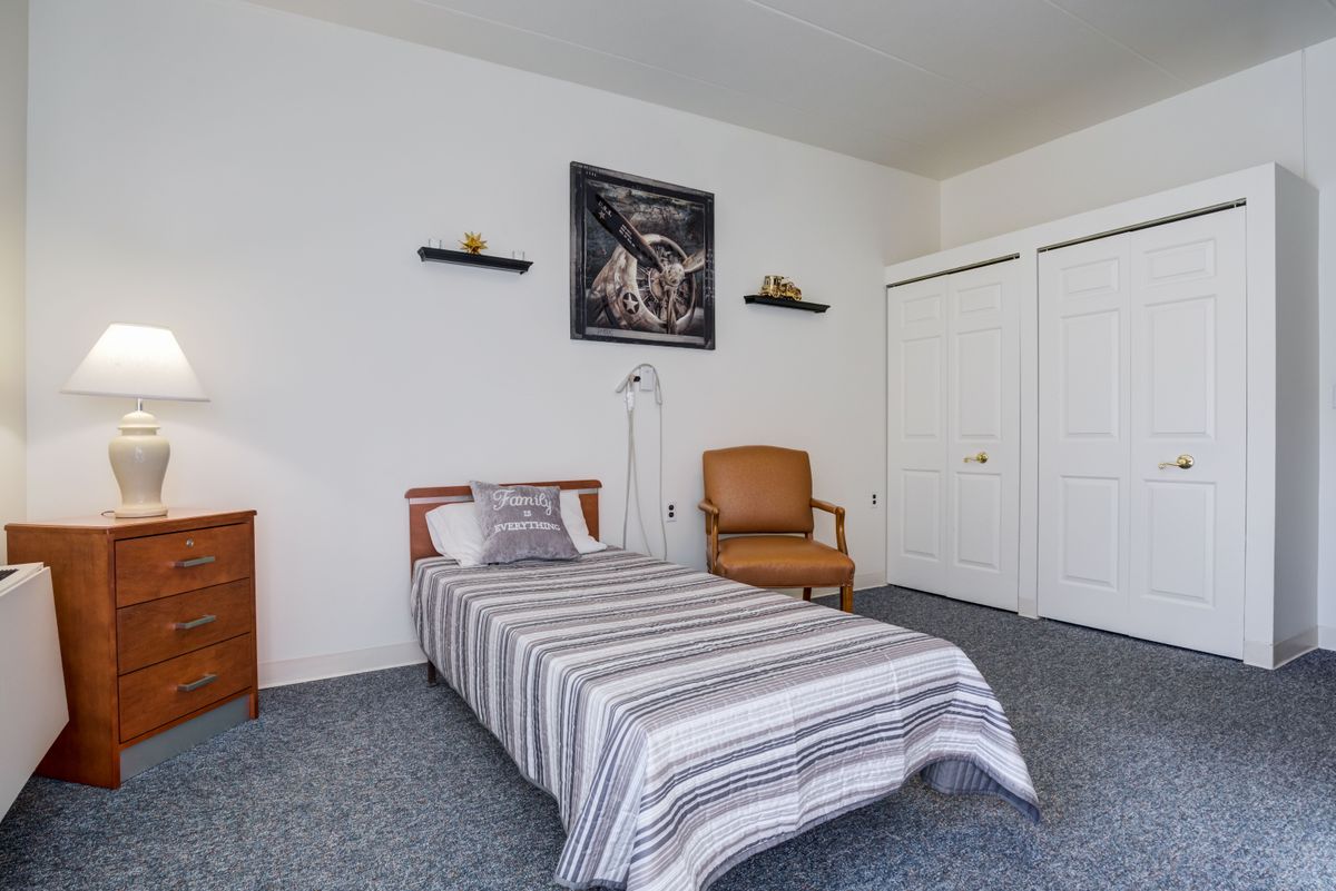 A minimalist bedroom with a single bed and striped bedding, featuring an armchair and wall art.