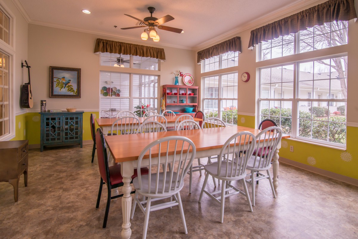 A bright and spacious dining room with a large table surrounded by chairs and multiple windows.