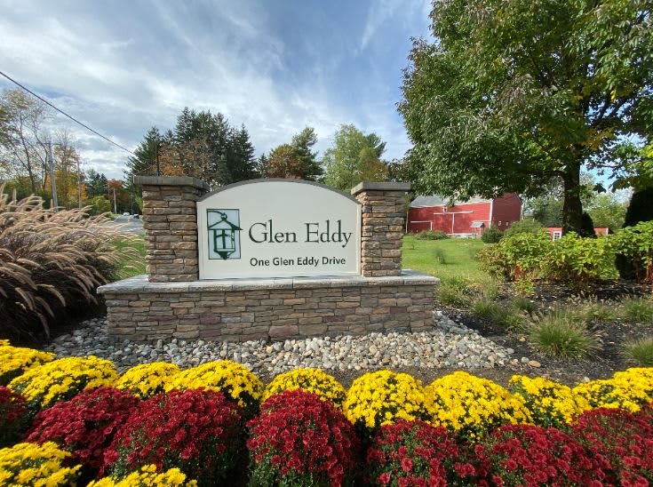 A stone sign for Glen Eddy surrounded by vibrant red and yellow flowers.