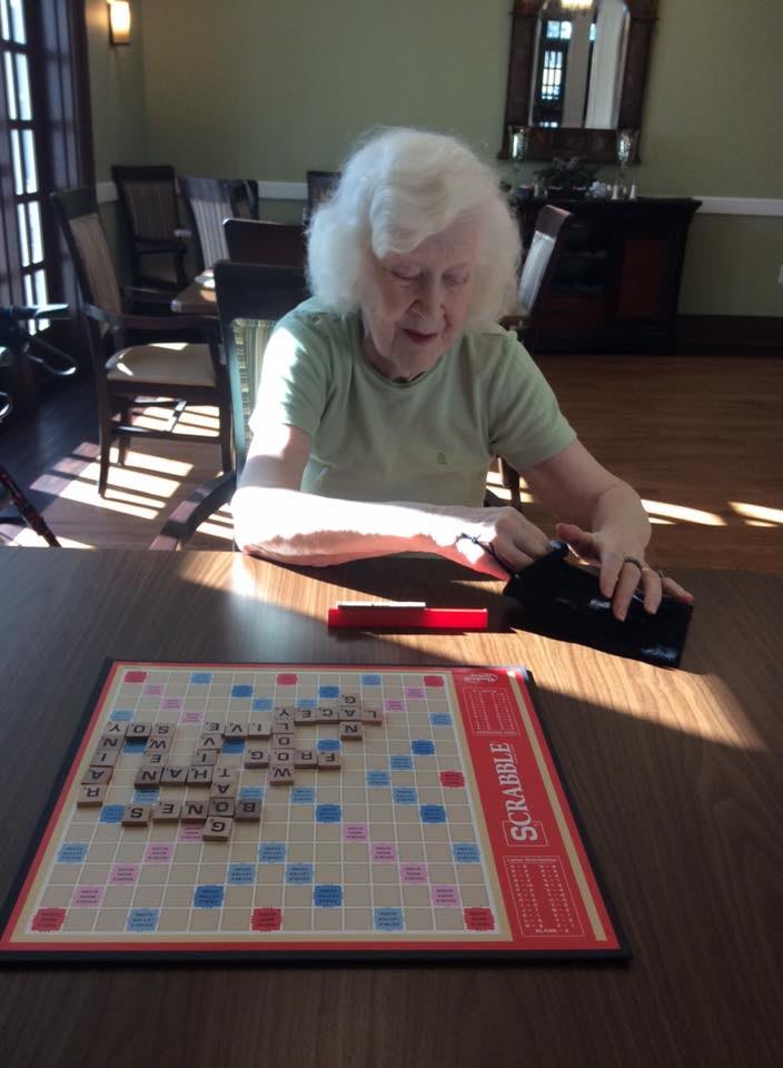 An elderly woman playing a game of Scrabble indoors during the day.
